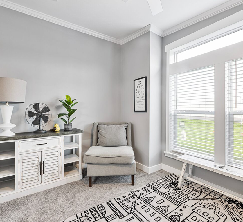 A cozy living space with a chair, stand, and bench by a large bright window.