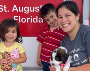 Woman and two children playing with a puppy.