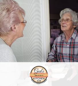 An elderly woman handing food to another elderly woman.