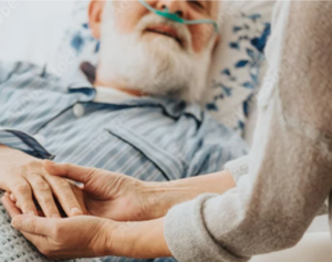 A man in a hospice bed holding hands with a loved one.