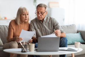Senior couple reviewing household bills and financial documents together on a laptop at home