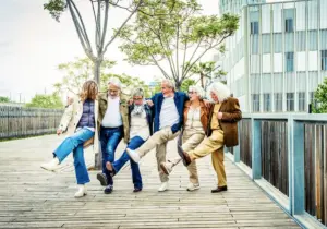 A group of elderly adults with their arms wrapped around each other's shoulders, kicking up their legs in a dance.