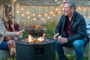 A middle aged man and woman sitting on either side of a fire pit having pleasant conversation.