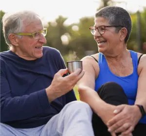 An elderly couple, outdoors sharing a hot cup of liquid (maybe tea or coffee).