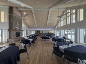 Spacious Silver Bay clubhouse with tables, chairs, large windows, and a stone fireplace in an open gathering area.