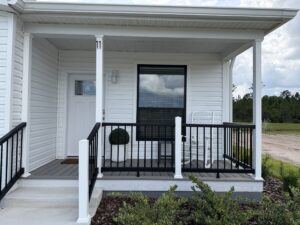 Front porch and entryway of a Silver Bay home with white siding, black railings, and landscaped shrubs.