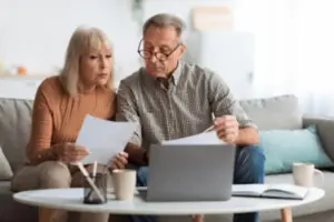 Senior couple reviewing household bills and financial documents together on a laptop at home