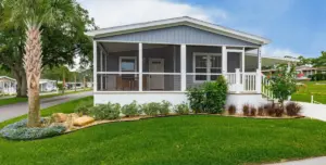 Silver Bay Palatka's Silver Springs 5006 manufactured home with gray siding, a white-trimmed screened porch, front lawn, palm tree, and landscaped garden beds.