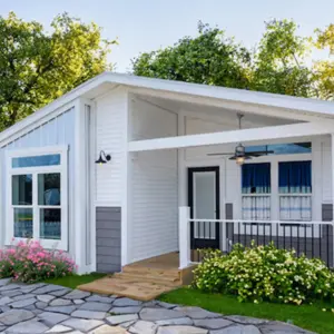 White Silver Bay home with a covered front porch, black railing, large windows, landscaped flower beds, and stone walkway.
