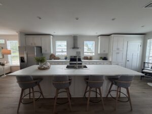 Open-concept kitchen in a Silver Bay manufactured home with white cabinetry, stainless steel appliances, a large island, and four bar stools.