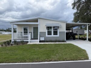Gray and white manufactured home at Silver Bay Palatka with a covered front porch, driveway, and carport.